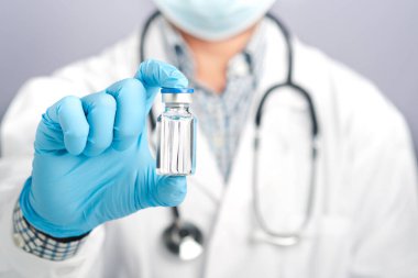 Doktor gri arka planda aşı şişesi gösteriyor. Bağışıklık aşısı ve virüs enfeksiyonuna karşı tedavi. Yakın plan fotoğraf. Tıbbi konsept ve virüse karşı savaş.