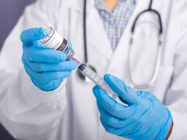 Beyaz üniformalı bir doktor, şırınga tutan tıbbi eldivenler ve aşı hazırlamak için COVID-19 aşı şişesi. Bağışıklık aşısı ve koronavirüs enfeksiyonu tedavisi.