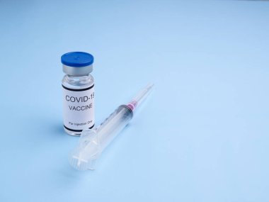 Cam şişedeki COVID-19 aşısı açık mavi arka planda bir şırıngayla yerleştirilmiş. Bağışıklık aşısı ve koronavirüs enfeksiyonunun tedavisi. Üst Manzara. Tıbbi ve sağlık hizmetleri kavramı.