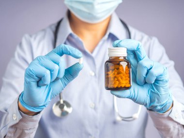 Yüz maskesi takan bir doktor, mavi eldiven giyen bir el, ve hastanede dururken ilaç ve ilaç şişesi tutan bir doktor. Sağlık ve Tıp Konsepti.