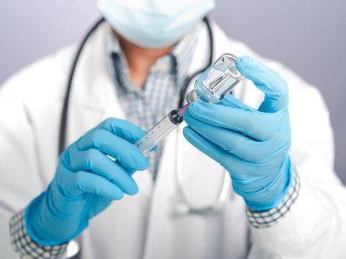 Beyaz üniformalı bir doktor, maske, şırınga tutan tıbbi eldivenler ve aşı için aşı şişesi. Virüs enfeksiyonuna karşı aşı ve tedavi.