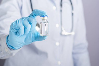Doktor gri arka planda dururken aşı şişesini gösteriyor. Bağışıklık aşısı ve virüs enfeksiyonuna karşı tedavi. Tıbbi konsept ve virüse karşı savaş.