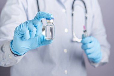 Doktor el ele tutuştuğu aşı şişesiyle şırıngayı gri arka planda tutuyor. Bağışıklık aşısı ve virüs enfeksiyonuna karşı tedavi. Tıbbi konsept ve virüse karşı savaş.
