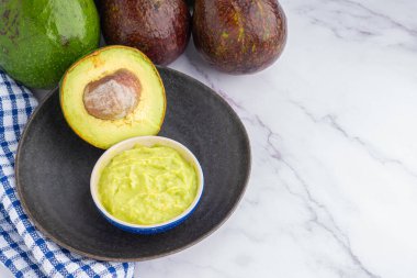 Tohumlu organik avokado, avokado yarımları ve siyah bir tabakta mermer bir masada kumaşla taze guacamole. Üst Manzara. Mesaj için yer var. Düz yatış stili. Sağlıklı meyve kavramı..