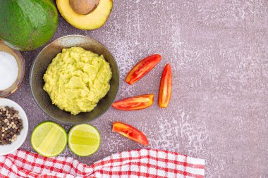 Tohumlu organik avokado, avokado yarımları, tüm meyve ve gri taşlı arka planda küçük bir tabakta tuz ve biberli taze guacamole. Üst Manzara. Sağlıklı meyve kavramı.