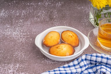Siyah bir tabakta limon jöleli kurabiyeler ve gri taşlı arka planda bir fincan çay. Madeleine - ev yapımı geleneksel Fransız küçük kurabiyesi. Mesaj için yer var. Deniz kabuğu tatlı kekleri.