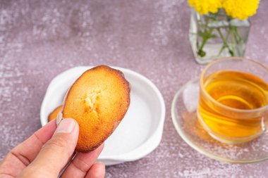 Bir tabakta limon jöleli bir madeleine ile gri taştan bir fonda bir fincan çay tutarken. Madeleine - ev yapımı geleneksel Fransız küçük kurabiyesi.