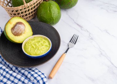 Tohumlu organik avokado, avokado yarımları ve siyah bir tabakta mermer zemin üzerinde kumaş ve çatal bıçakla taze guacamole. Üst Manzara. Mesaj için yer var. Sağlıklı meyve kavramı.