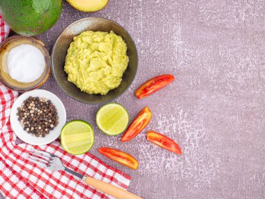 Tohumlu organik avokado, avokado yarımları, tüm meyve ve gri taşlı arka planda küçük bir tabakta tuz ve biberli taze guacamole. Üst Manzara. Sağlıklı meyve kavramı.