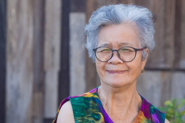 Senior woman wearing eyeglasses with short white hair smiling and looking at camera while standing in a garden. Concept of old people and healthcare.