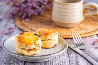 Geleneksel İngiliz çörekleri bir tabakta, ahşap bir masada çay fincanı ve mor çiçekli bulanık bir arka plan..