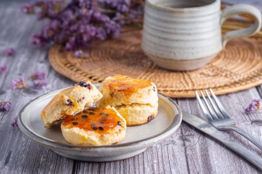 Geleneksel İngiliz çörekleri bir tabakta, ahşap bir masada çay fincanı ve mor çiçekli bulanık bir arka plan..