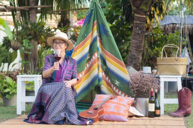 Üst düzey bir kadın elinde kırmızı şarap kadehi olan bir şapka takıyor, bahçede bir sandalyede otururken gülümsüyor ya da çadır arka planında Bohem tarzı bir çadırda oturuyor. Yaşlılar ve rahatlama kavramı.