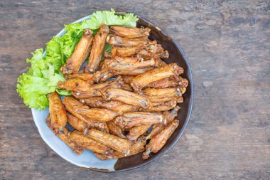 Fried chicken wings with fish sauce with salad vegetables on a white plate placed on a wooden table. Close-up photo. Space for text. Concept of foods.