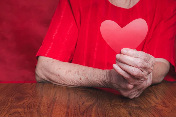 Red paper cut heart shape hold by hand senior woman. Valentine\'s day. Concept of aged people and love.