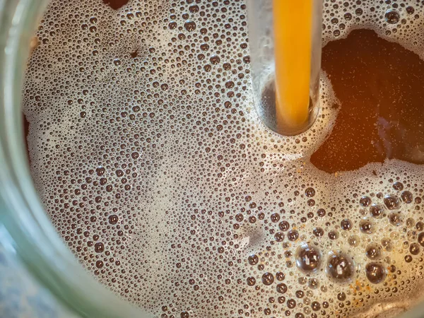 Close-up of craft beer and foam in a fermentation container. Process of making home beer from malt. Craft beer from barley and dark malt.