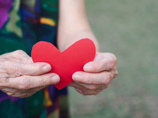手のシニア女性が持つ赤い紙カットハート型 バレンタインデーだ 高齢者と愛の概念 — ストック写真