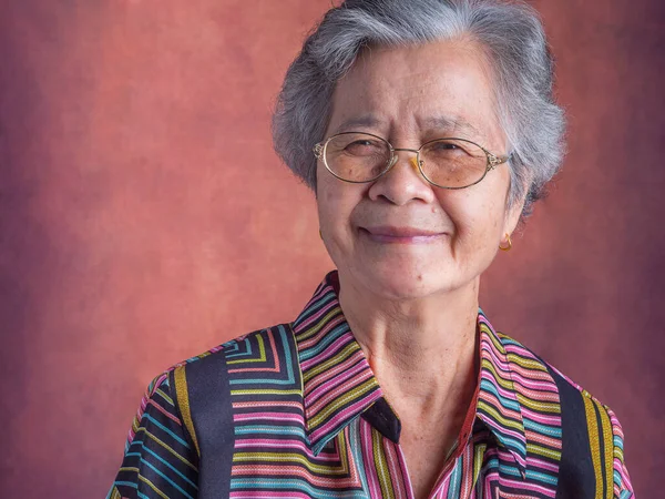 Portrait of a beautiful senior Asian woman wearing glasses with short white hair smiling and looking at the camera while standing with a vintage background. Concept of aged people and healthcare.