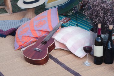 Renkli kumaşlardan yapılmış bir çadırla dekore edilmiş ve ukulele, yastık, bez, çiçek, kuru vazo, paspas, cam ve şarap şişesiyle süslenmiş bir açık hava alanı. Rahatlama kavramı.