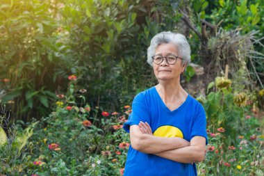 Senior woman with short gray hair arms crossed, smiling and looking at the garden. Concept of aged people and healthcare.