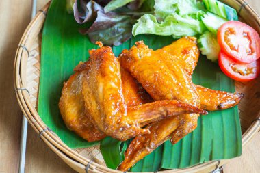 Chicken wing spicy, tomatoes, and lettuce on a banana leaf placed in a bamboo tray. Close-up photo.