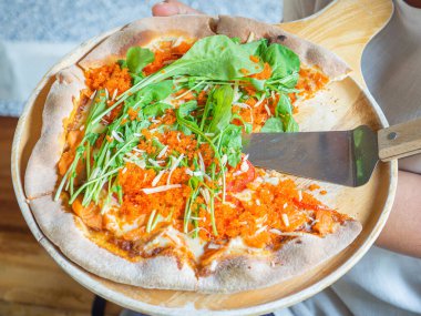 Pizza salmon and rocket consisted of tomato sauce, mozzarella cheese, smoked salmon, rocket, tomato, ebiko, parmesan cheese on a wooden plate placed on a wood table. Concept of healthy foods.