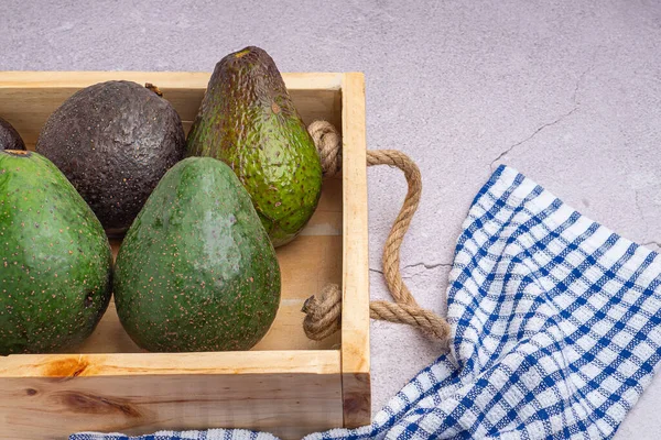 Avocados are placed in a wooden crate on a gray stone background. Space for text. Close-up photo. Concept of healthy fruits.