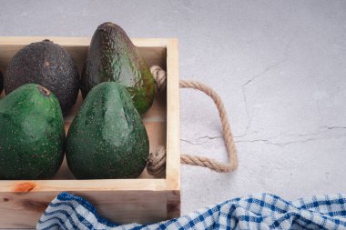Avocados are placed in a wooden crate on a gray stone background. Space for text. Close-up photo. Concept of healthy fruits.