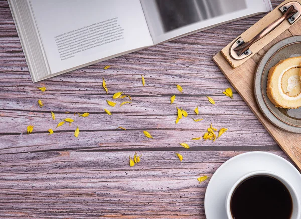 Top view of a book with roll cake on a plate on a wooden tray and a white coffee cup placed on a wooden table. Space for text. Concept of relaxation.