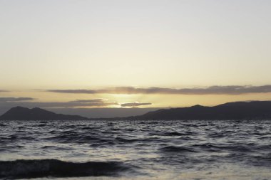 Denizde yaz günbatımı ve arka planda dağlar..