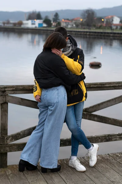 Deniz kenarında yürürken kucaklaşan bir çift, kalın kıyafetler giyiyorlar, arka plan bulanık..