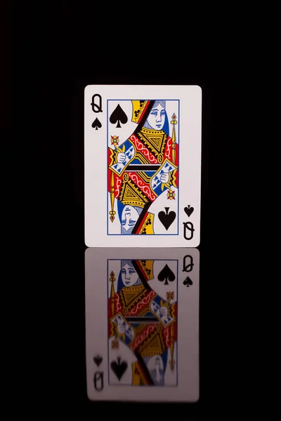 Playing card, queen of spades on a black background with reflection