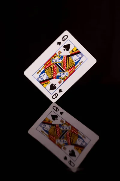 Playing card, queen of spades on a black background with reflection.