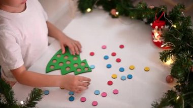 Kafasında yeni yıl şapkası olan beyaz tişörtlü bir kız çocuğu orijinal bir Noel ağacı ayırıcısını kesiyor. Noel gelenekleri konsepti. Montessori 'nin Noel' de gelişmiş motor becerileri