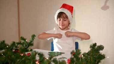 Kafasında yeni yıl şapkası olan beyaz tişörtlü bir kız çocuğu orijinal bir Noel ağacı ayırıcısını kesiyor. Noel gelenekleri konsepti. Montessori 'nin Noel' de gelişmiş motor becerileri