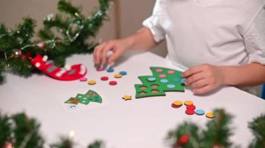 Kafasında yeni yıl şapkası olan beyaz tişörtlü bir kız çocuğu orijinal bir Noel ağacı ayırıcısını kesiyor. Noel gelenekleri konsepti. Montessori 'nin Noel' de gelişmiş motor becerileri