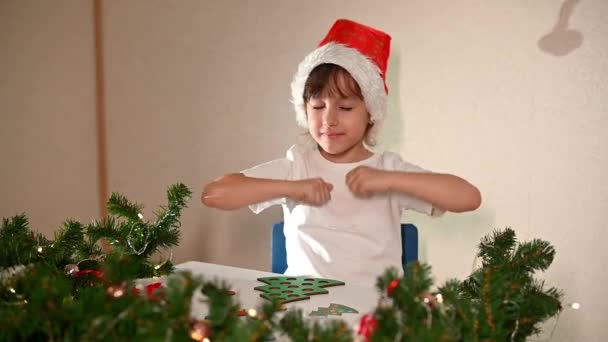 一个穿着白色T恤头戴新年帽的小女孩剪下了一个玩具圣诞树分拣器 圣诞节传统的概念 圣诞期间蒙台梭利运动技能的发展 — 图库视频影像