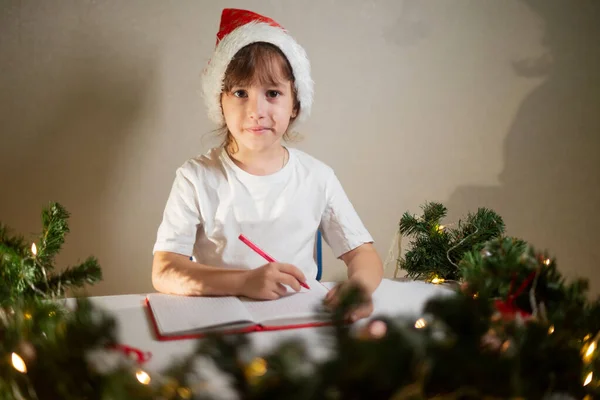 Dziewczynka Białej Koszulce Czerwonym Długopisem Czapką Noworoczną Głowie Pisze Mikołajowi — Zdjęcie stockowe