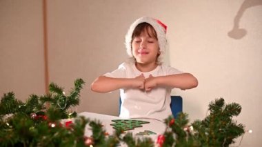 Kafasında yeni yıl şapkası olan beyaz tişörtlü bir kız çocuğu orijinal bir Noel ağacı ayırıcısını kesiyor. Noel gelenekleri konsepti. Montessori 'nin Noel' de gelişmiş motor becerileri