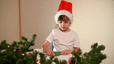 Kafasında yeni yıl şapkası olan beyaz tişörtlü bir kız çocuğu orijinal bir Noel ağacı ayırıcısını kesiyor. Noel gelenekleri konsepti. Montessori 'nin Noel' de gelişmiş motor becerileri