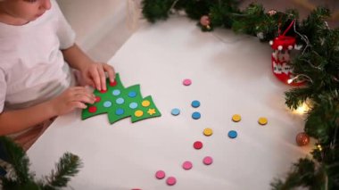 Kafasında yeni yıl şapkası olan beyaz tişörtlü bir kız çocuğu orijinal bir Noel ağacı ayırıcısını kesiyor. Noel gelenekleri konsepti. Montessori 'nin Noel' de gelişmiş motor becerileri