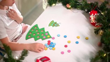 Kafasında yeni yıl şapkası olan beyaz tişörtlü bir kız çocuğu orijinal bir Noel ağacı ayırıcısını kesiyor. Noel gelenekleri konsepti. Montessori 'nin Noel' de gelişmiş motor becerileri.
