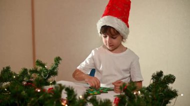 Kafasında yeni yıl şapkası olan beyaz tişörtlü bir kız çocuğu orijinal bir Noel ağacı ayırıcısını kesiyor. Noel gelenekleri konsepti. Montessori 'nin Noel' de gelişmiş motor becerileri