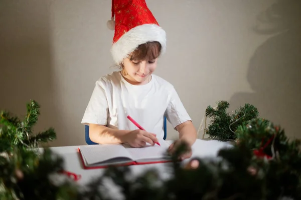 Dziewczynka Białej Koszulce Czerwonym Długopisem Czapką Noworoczną Głowie Pisze Mikołajowi — Zdjęcie stockowe