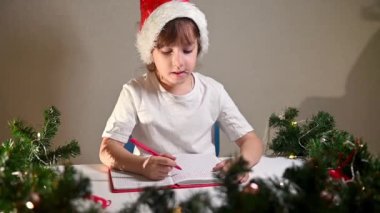 Beyaz tişörtlü, kırmızı kalemli ve başında yeni yıl şapkası olan bir kız çocuğu doğum beklentisiyle masaya sevgili Noel Baba 'ya bir mektup yazıyor. Yeni yıl için hediye listesi