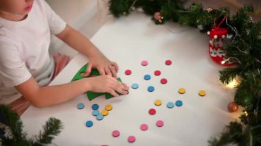 Kafasında yeni yıl şapkası olan beyaz tişörtlü bir kız çocuğu orijinal bir Noel ağacı ayırıcısını kesiyor. Noel gelenekleri konsepti. Montessori 'nin Noel' de gelişmiş motor becerileri