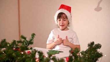 Kafasında yeni yıl şapkası olan beyaz tişörtlü bir kız çocuğu orijinal bir Noel ağacı ayırıcısını kesiyor. Noel gelenekleri konsepti. Montessori 'nin Noel' de gelişmiş motor becerileri