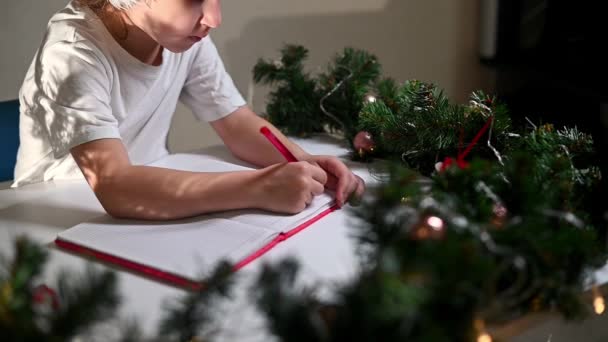身穿白色T恤 头戴红笔 头戴新年帽的女孩在桌上给亲爱的圣诞老人写了一封信 希望他早产 愿新年礼物的清单 — 图库视频影像