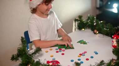 Kafasında yeni yıl şapkası olan beyaz tişörtlü bir kız çocuğu orijinal bir Noel ağacı ayırıcısını kesiyor. Noel gelenekleri konsepti. Montessori 'nin Noel' de gelişmiş motor becerileri