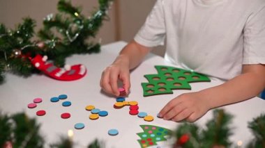 Kafasında yeni yıl şapkası olan beyaz tişörtlü bir kız çocuğu orijinal bir Noel ağacı ayırıcısını kesiyor. Noel gelenekleri konsepti. Montessori 'nin Noel' de gelişmiş motor becerileri